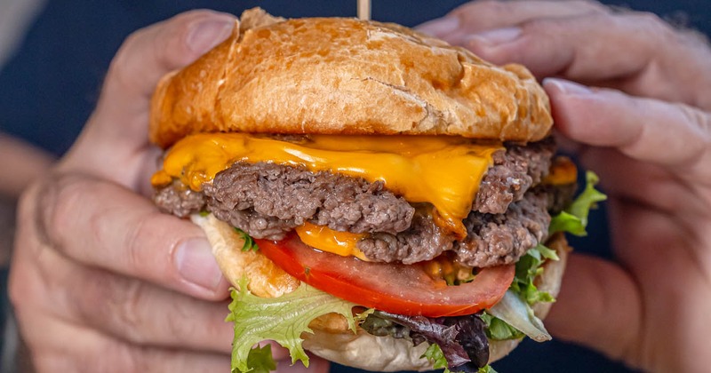 Hand holding a double cheeseburger with melted cheese