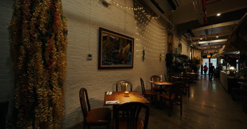 Dimly lit interior with brick walls, fairy lights, a painting, tables, chairs and decorative flowers