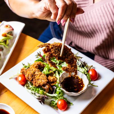 A person lifting a fried soft-shell crab above a salad with dipping sauce.