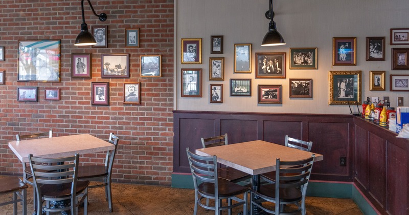 Cozy interior seating area with two tables for four guests by the wall with framed photos