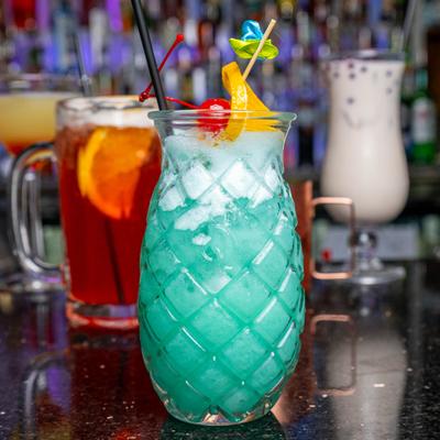 Blue Lagoon cocktail served in pineapple-shaped glass, alongside other cockatils.
