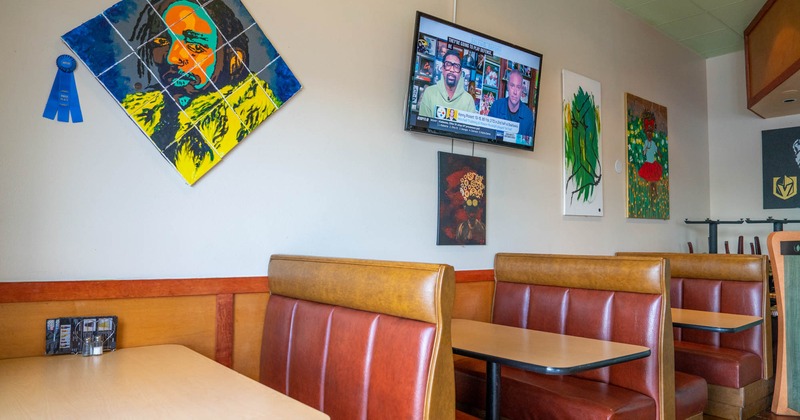 Restaurant booths by a wall with artworks and a TV