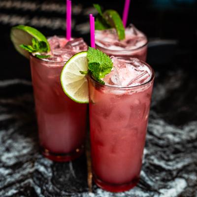 Three pink cocktails served over ice, garnished with fresh lime and mint.