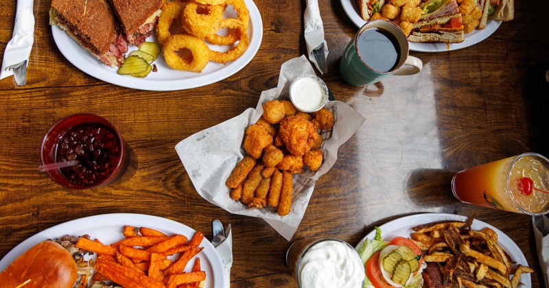 Various sandwiches with sides and a appetizer basket served alongside drinks