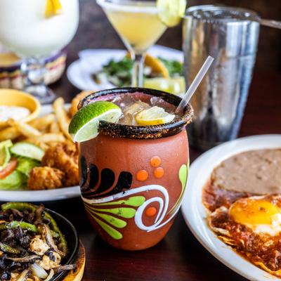 Cantarito cocktail served in a clay cup, served alongside other drinks and food.