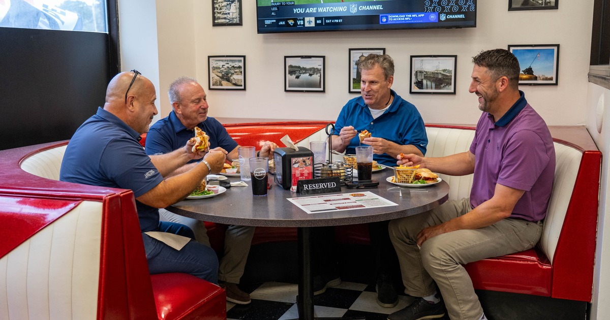 Four patrons eat food at a table beneath a television