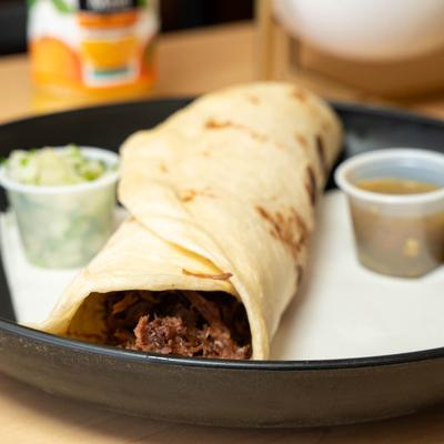 Barbacoa burrito served with onion cilantro cup and a cup of salsa on the side.