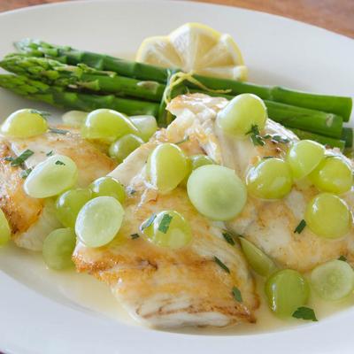 Sole filets served with a creamy white wine sauce, garnished with green grapes and asparagus.