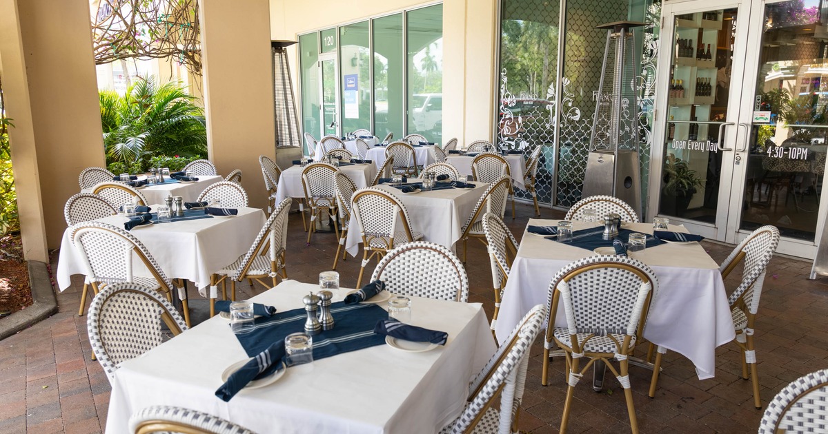 Outdoor dining area - white tablecloths, wicker chairs and glass windows.