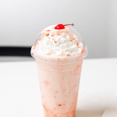 Milkshake topped with whipped cream and a cherry, served in a plastic cup.