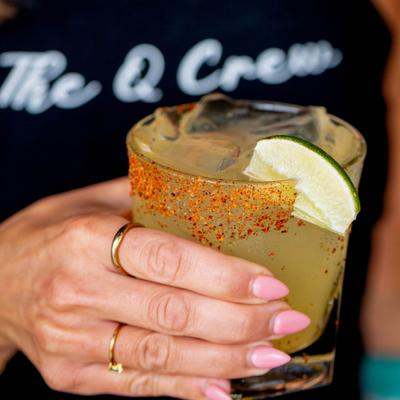 Hand holding a Margarita in a rock glass with a chili rim and a lime wedge.