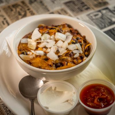 Bowl of chili topped with diced onions and served with two sauces on the side.