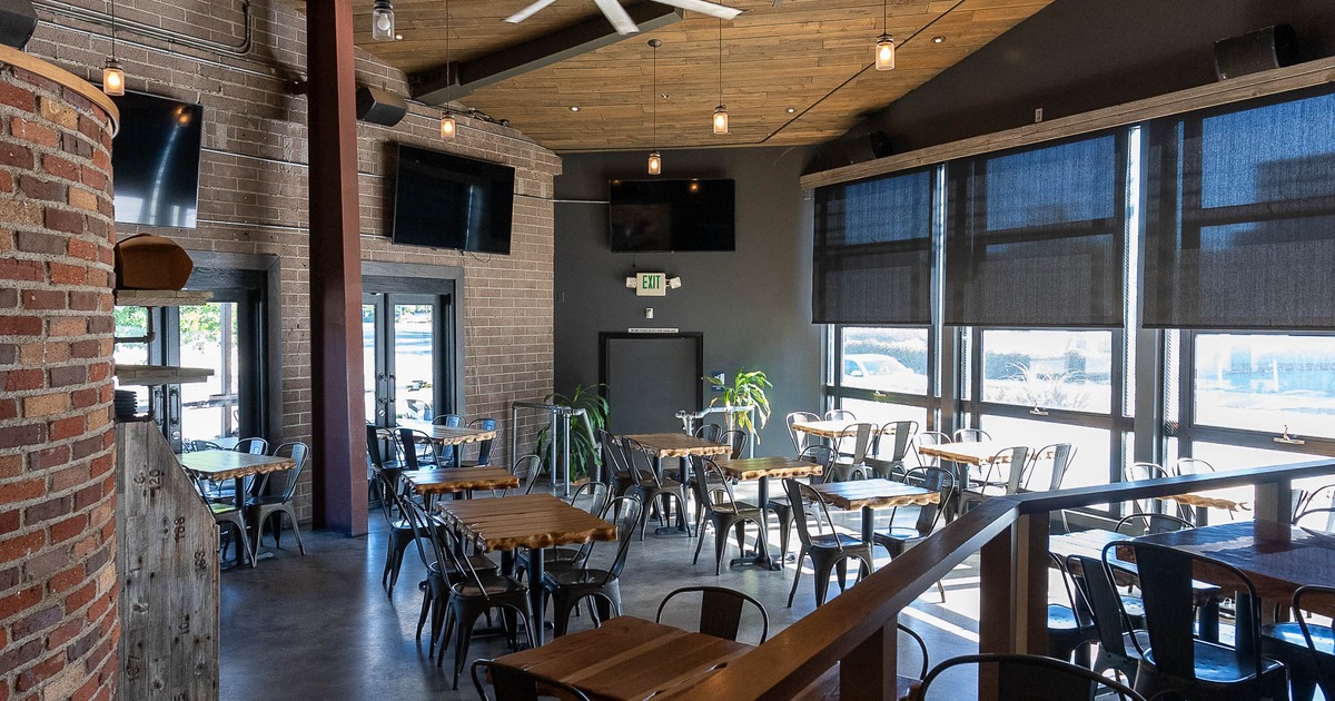 Modern interior - brick walls, wooden tables, metal chairs, a large ceiling fan and pendant lights