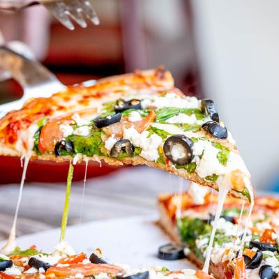 Greek pizza, a slice being lifted up with cheese strings, close up.