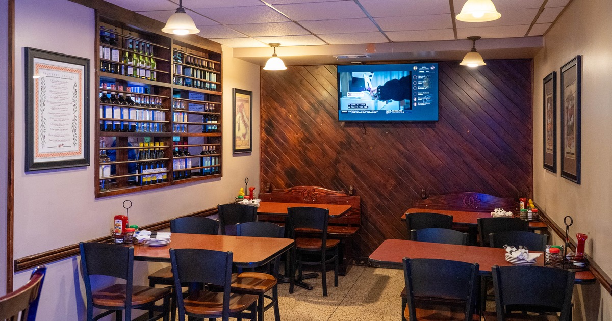 Interior of a restaurant with wooden tables, chairs, and a wall-mounted bottle rack