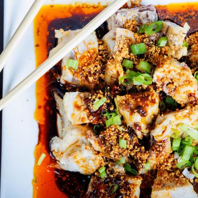 Spicy chili oil chicken with crushed peanuts and scallions served on a white plate.