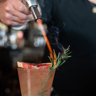 Cocktail with grapefruit garnish, and torched rosemary.