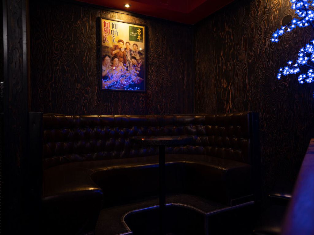 Private booth seating with vintage poster on the wall and blue light coming from a decorative tree