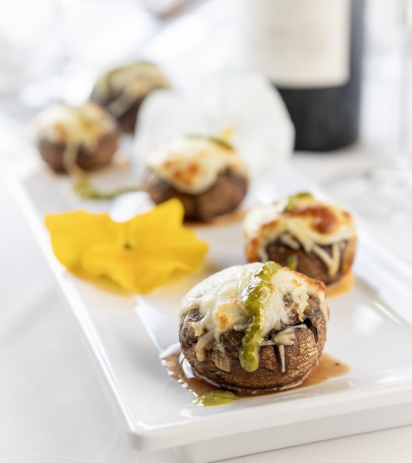 stuffed mushrooms on a white plate with a bottle of wine.