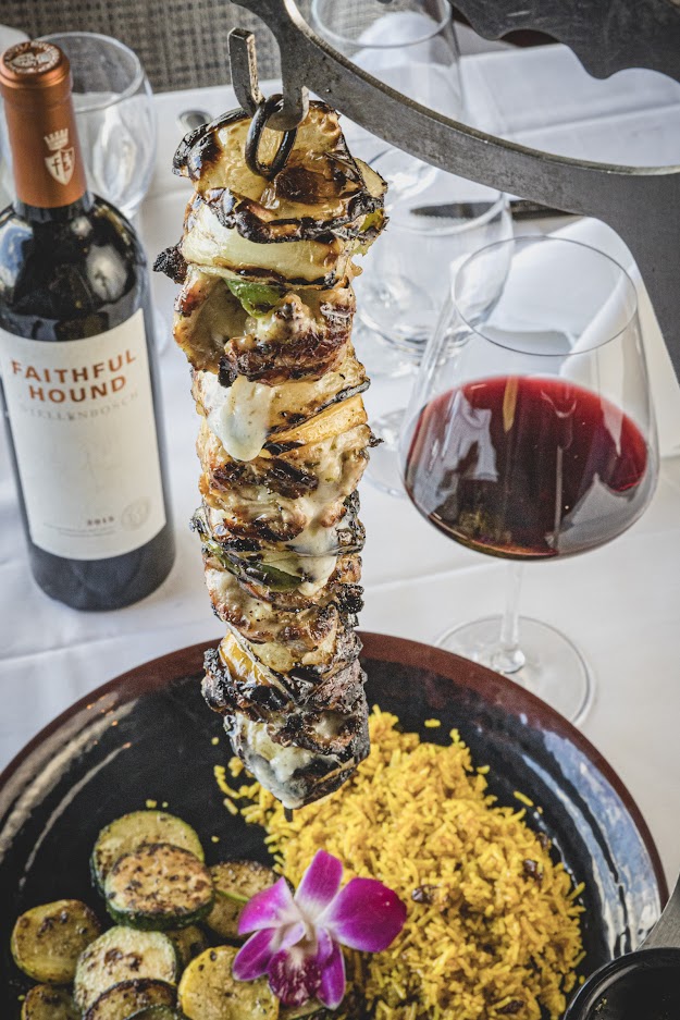a plate of skewered vegetables and wine on a table.