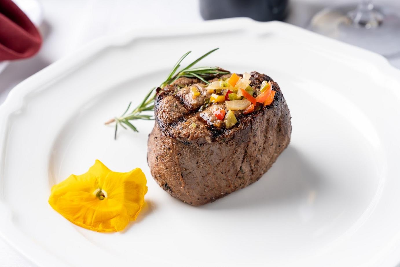 a steak on a white plate with a flower on it.