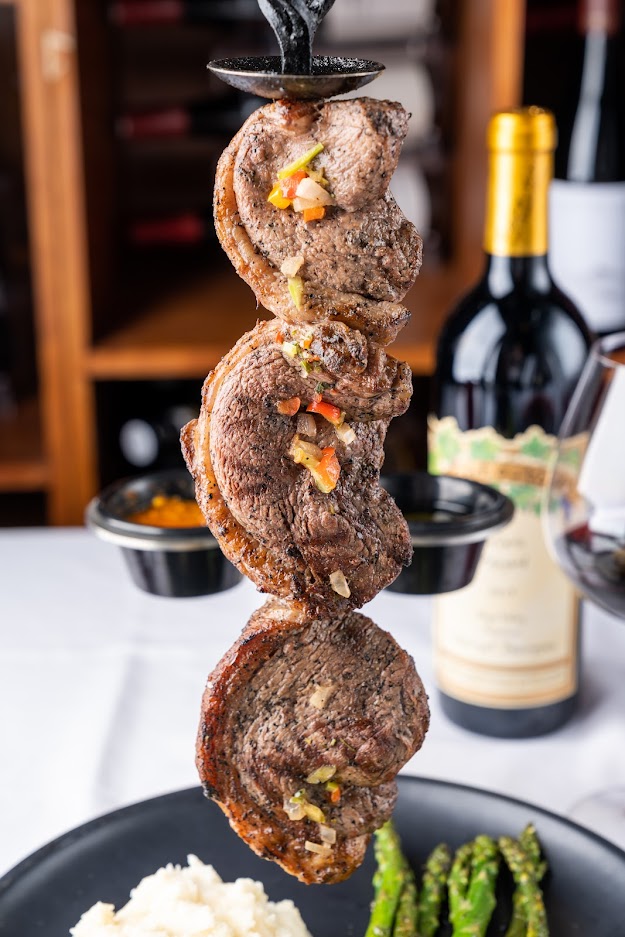 steak skewers on a plate with asparagus and a bottle of wine.