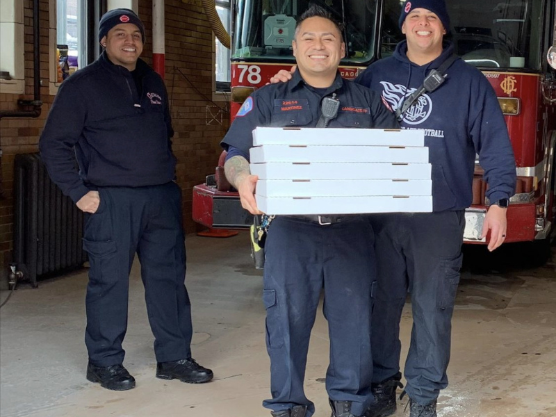 Smiling firefighters posing for the photo with delivered pizzas