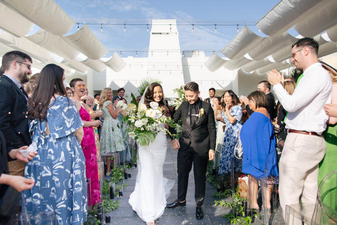 Newly weds are walking across the aisle while guests are applauding