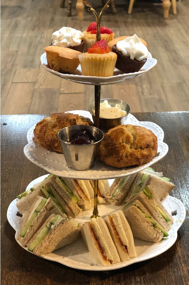 A tiered serving tray filled with cupcakes, scones, and sandwiches on a table in a tea room.