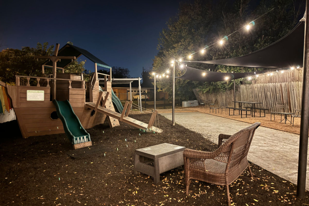 An outdoor play area illuminated by string lights at dusk, featuring a wooden playset.