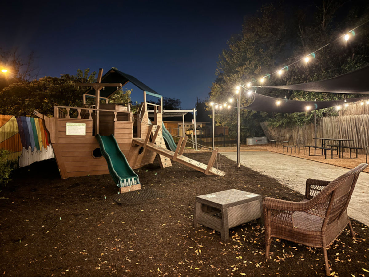 An outdoor seating area at night with a playground and string lights.