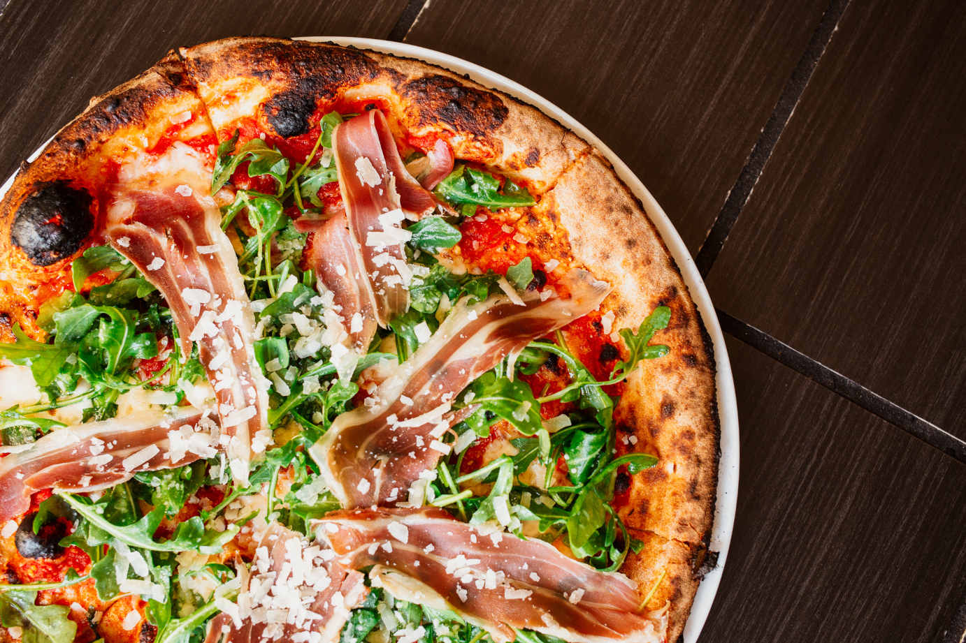 A pizza topped with cheese, prosciutto and arugula