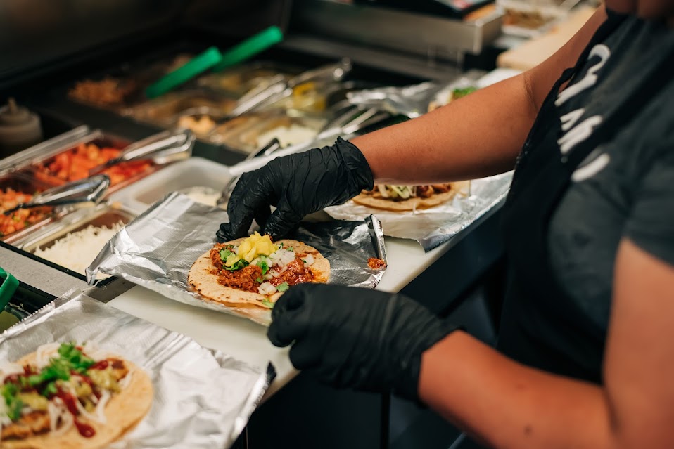 Taco bar, staff putting topping on a tortilla