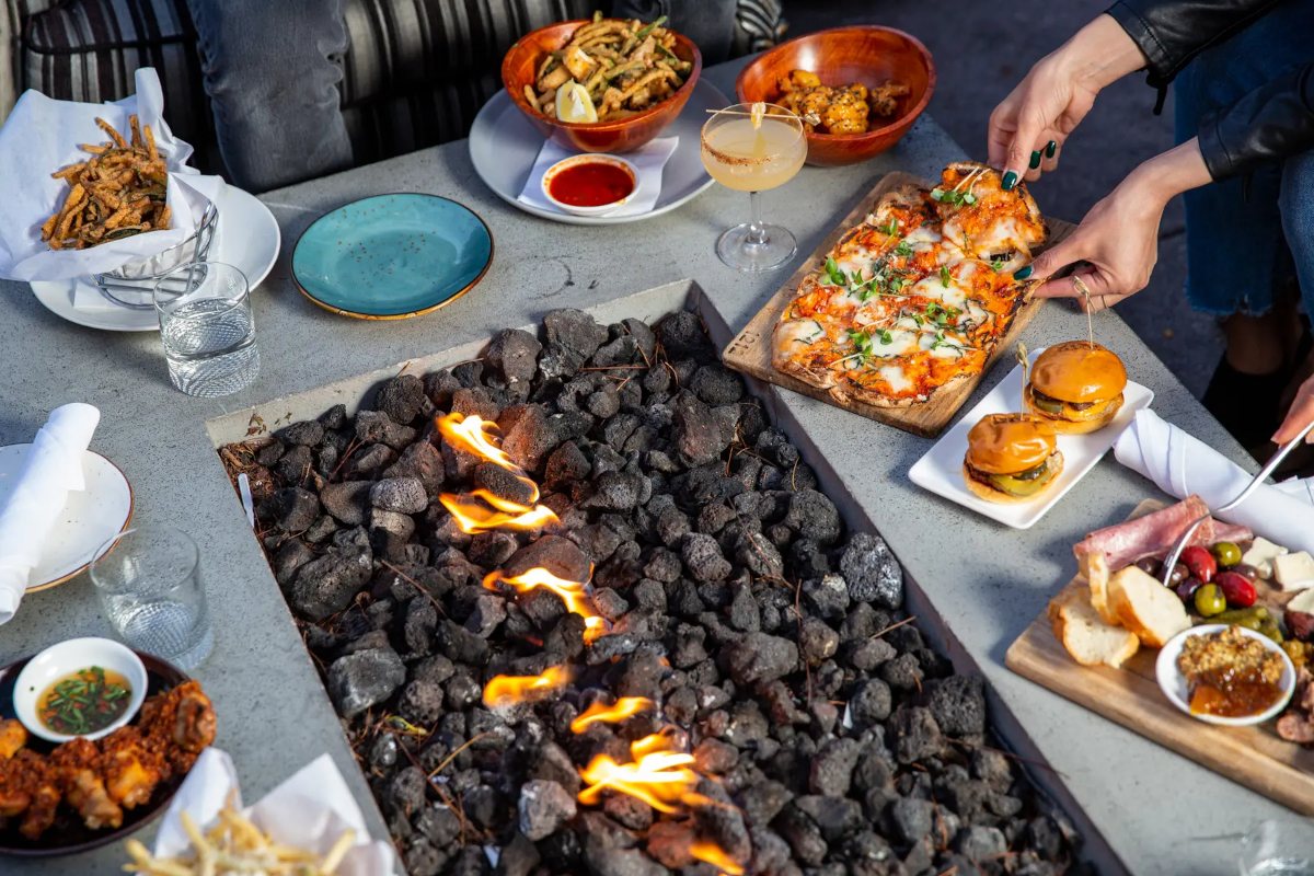 Different dishes on a fire pit table, guests dining