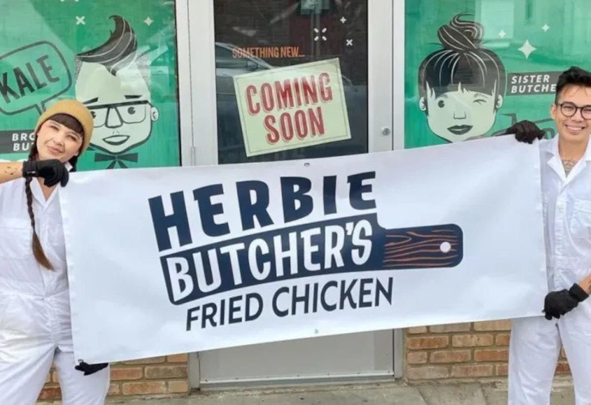 Aubry and Kale hold a white with black print banner, “Herbie’s Fried Chicken”