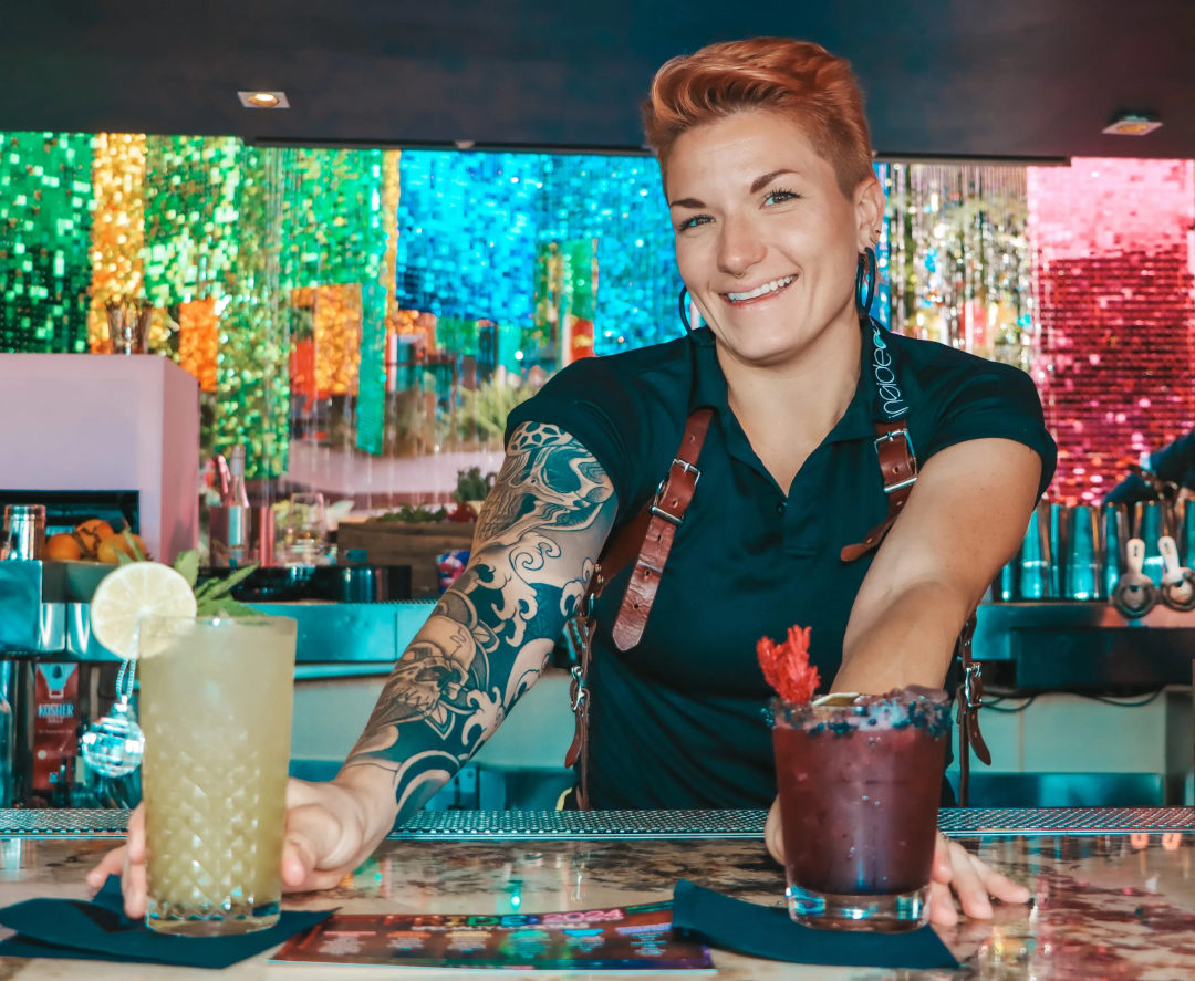A person standing in a bar holding two coctails