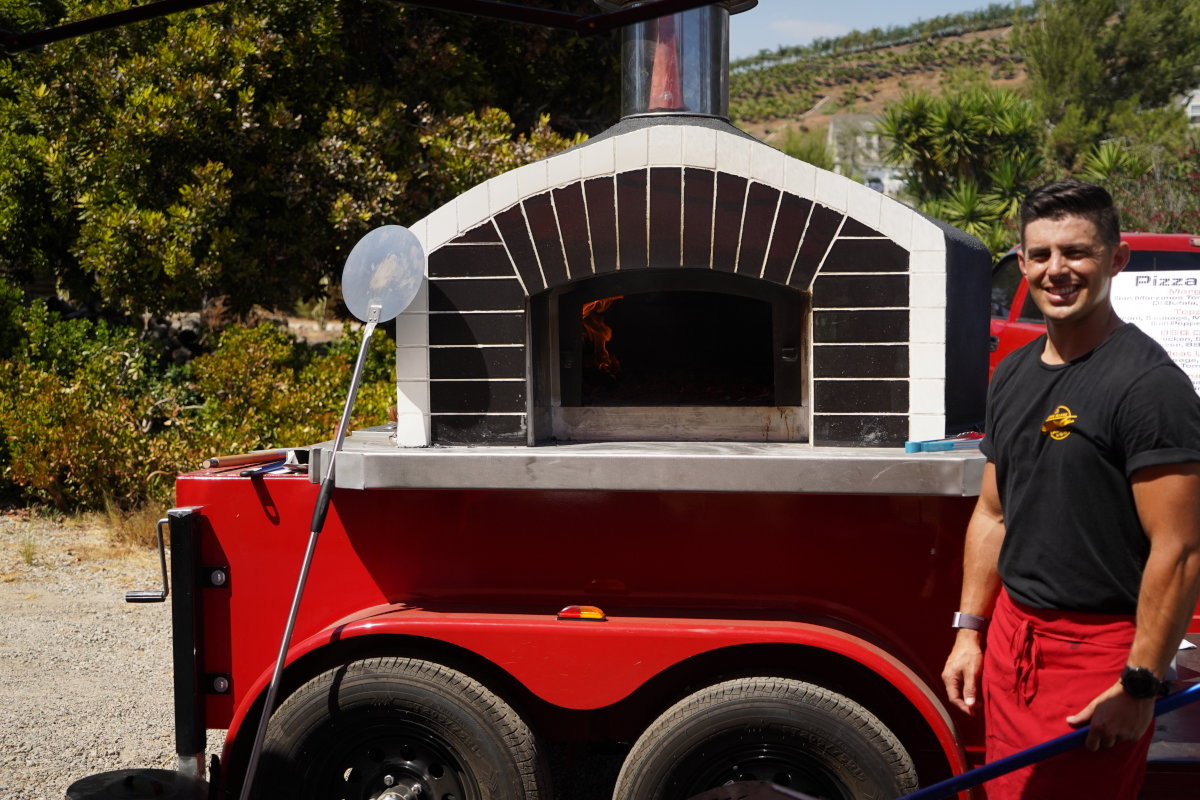 Outdoor shot of employee standing by mobile pizza oven