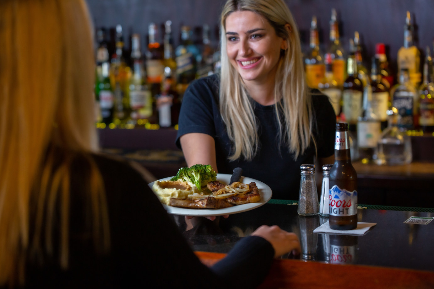 Employee serving a guest with pork chops and a beer