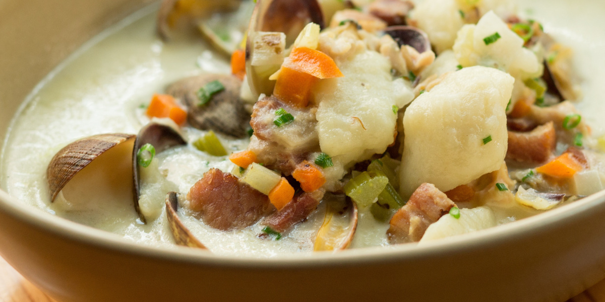a bowl of soup with clams, potatoes and carrots.
