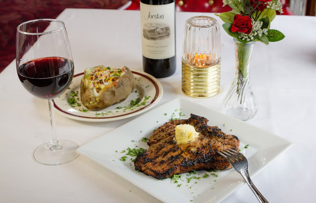 Prime bone in ribeye served with steak, baked potatoes and glass of wine