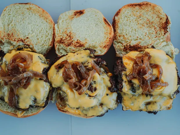 Three cheeseburgers with melted cheese and caramelized onions on toasted buns.