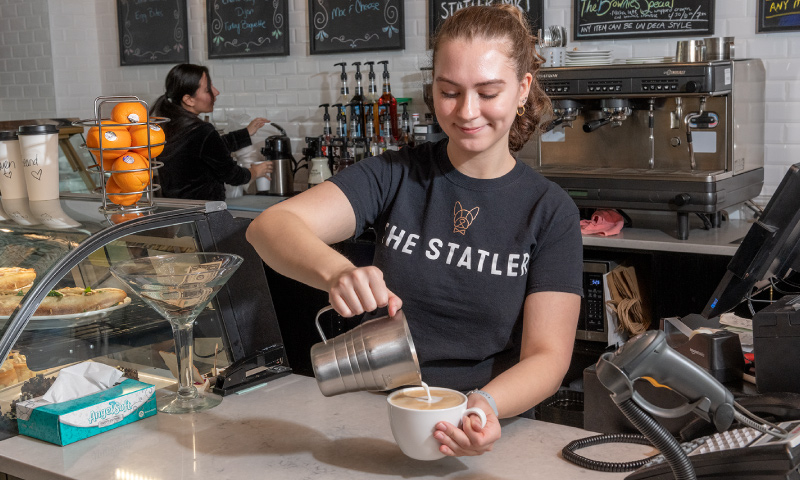 A staff member pouring milk into a cup of coffee behind counter