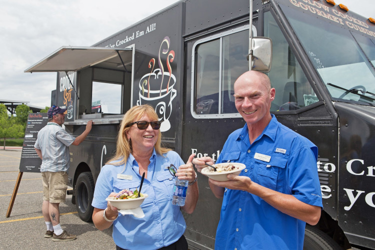 Two guests holding food and smiling in front of the foodtruck