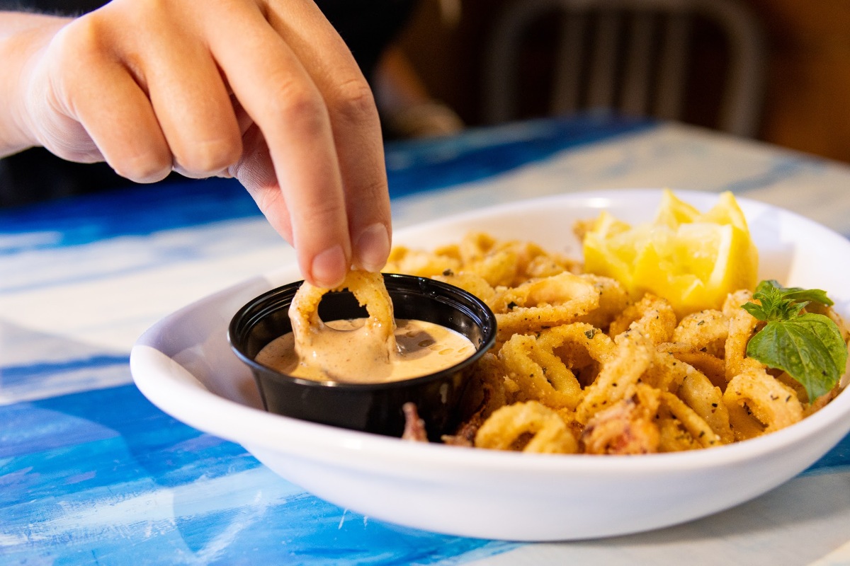 A hand dipping deep fried calamari into a creamy sauce