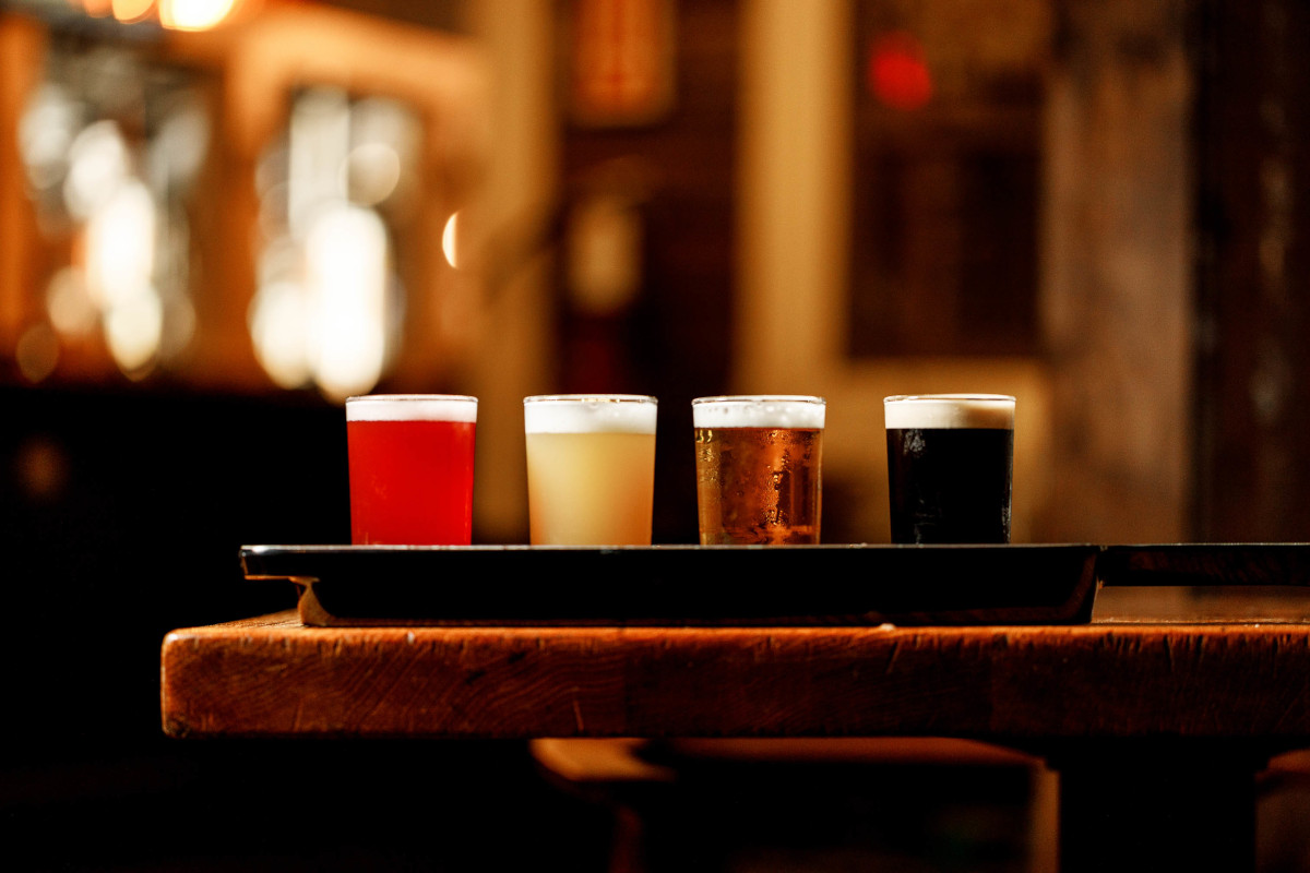 Four beer-tasting glasses in different colors on a tray in a dimly lit bar