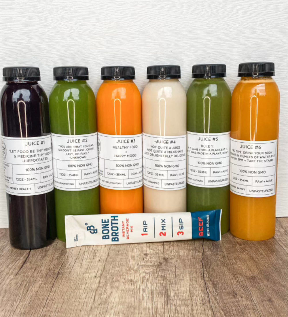 Seven colorful juice bottles lined up on a wooden surface.