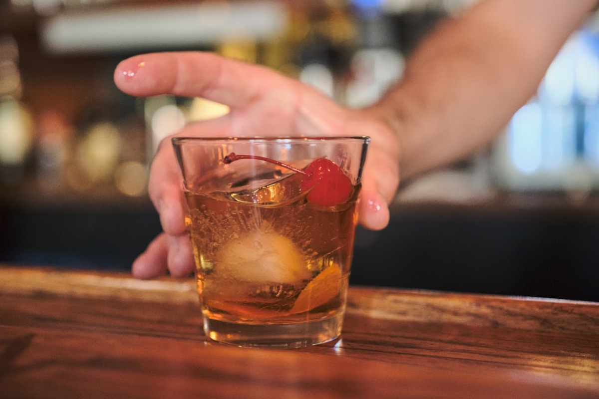 Bartender's hand serving a glass of Old Fashioned cocktail at the bar