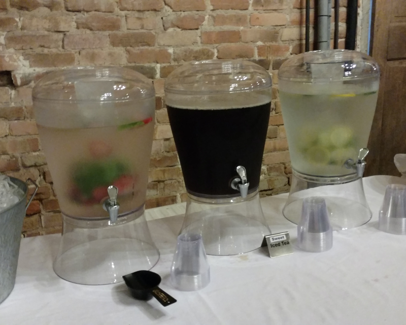 three drink dispensers are lined up on a table.