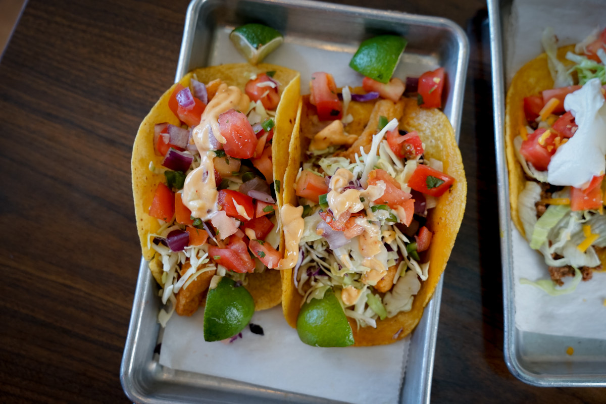 a plate of two tacos with vegies, sauce and lime