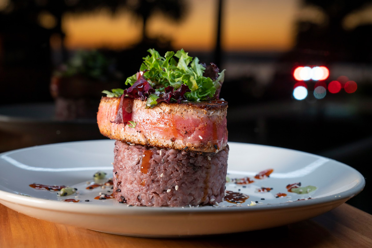 Blackened tuna steak atop rice, garnished with mixed lettuce 